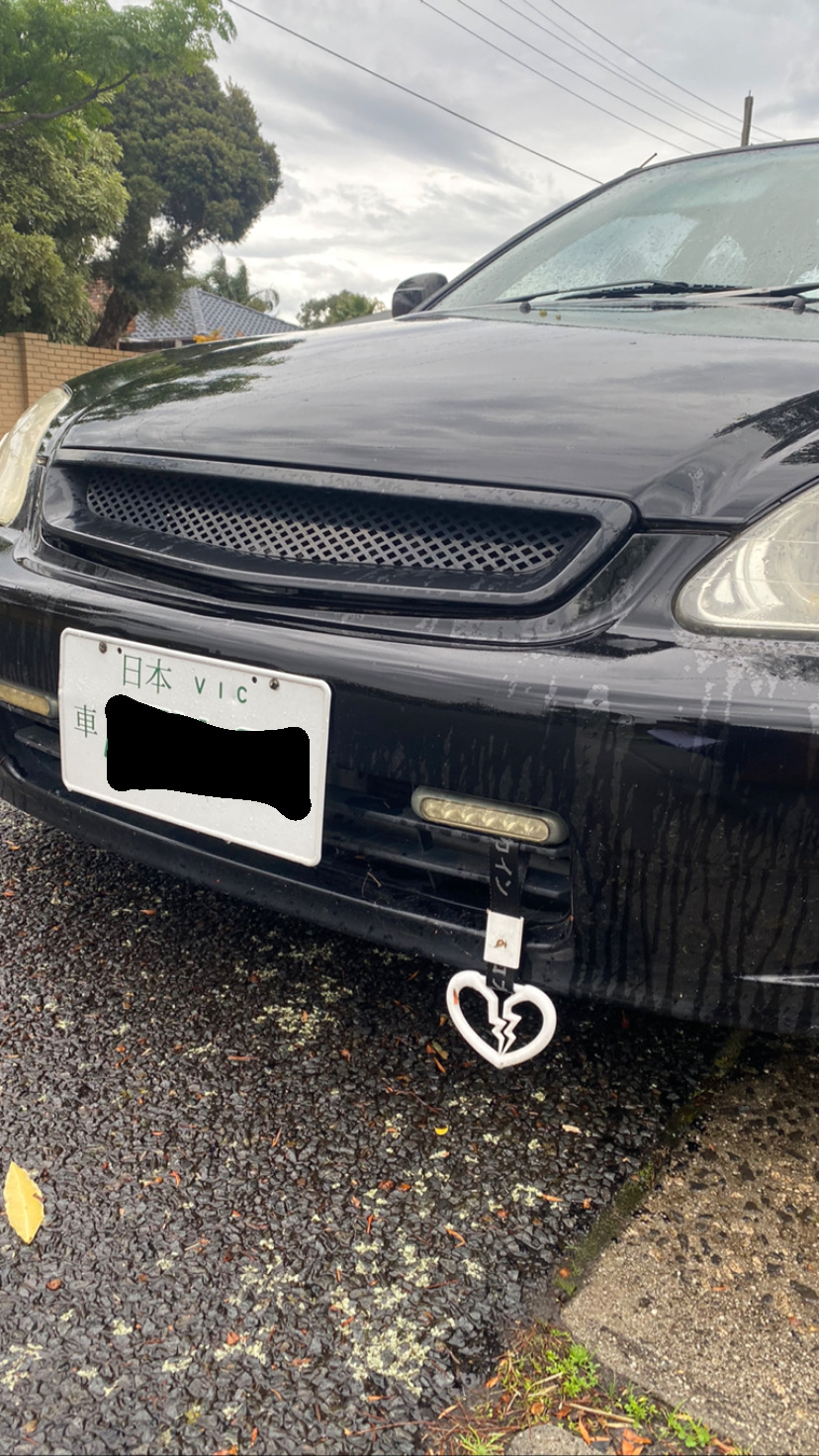 Black car with plastic broken heart hanging from the front grill.